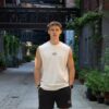 Model draagt de witte KMKG Tee met KMKG logo, voorkant tank, casual look in een stedelijke setting